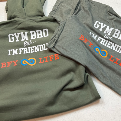 Picture of a military green sweatshirt and heather military green crewneck laying on a table
